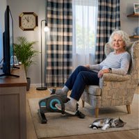 Seniorin nutzt den Pedaltrainer für Senioren bequem im Sessel vor dem Fernseher